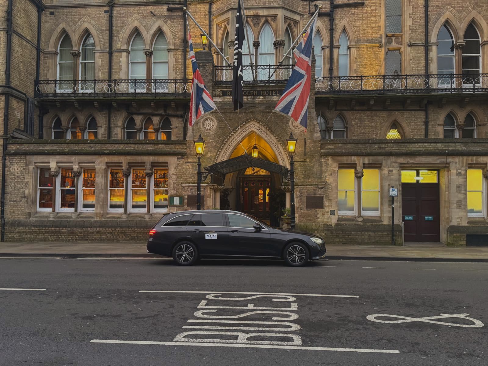 A black Mercedes E-Class Estate parked outside the Randolph Hotel in Oxford at dusk