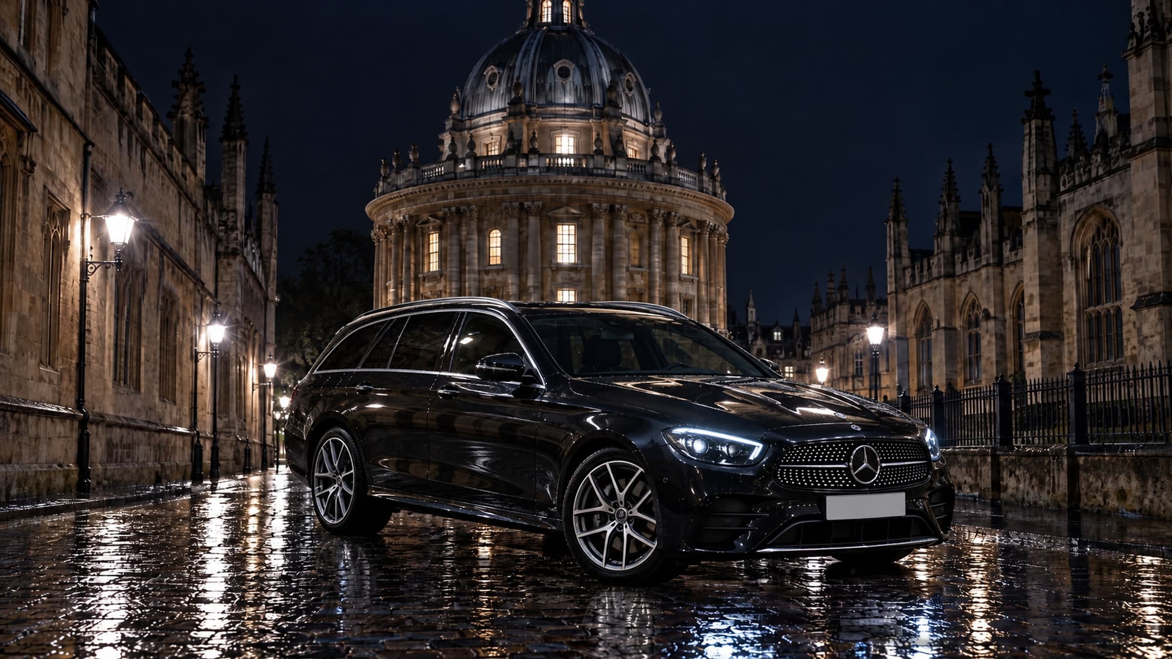 A black Mercedes E-Class Estate parked on the wet cobbles of Radcliffe Square in Oxford at night, headlights on, the Radcliffe Camera lit behind it
